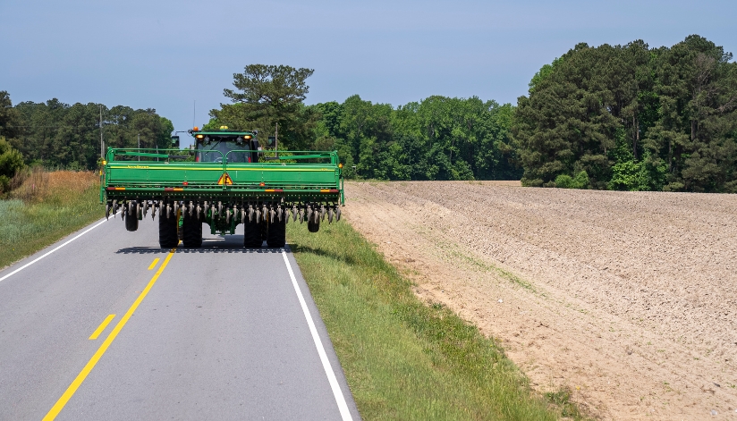 Wide farm tractor traveling on a rural Wisconsin road beside a field.