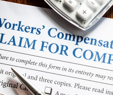 Close-up of a workers’ compensation claim form with a pen, calculator, paper clip, and eyeglasses on a wooden desk.