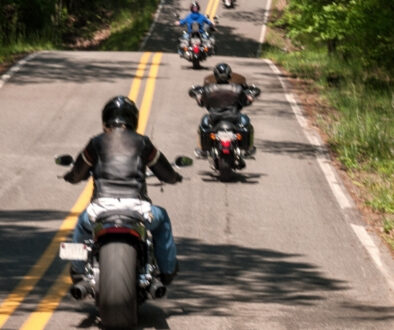 Several motorcyclists riding along a winding two-lane road surrounded by trees.