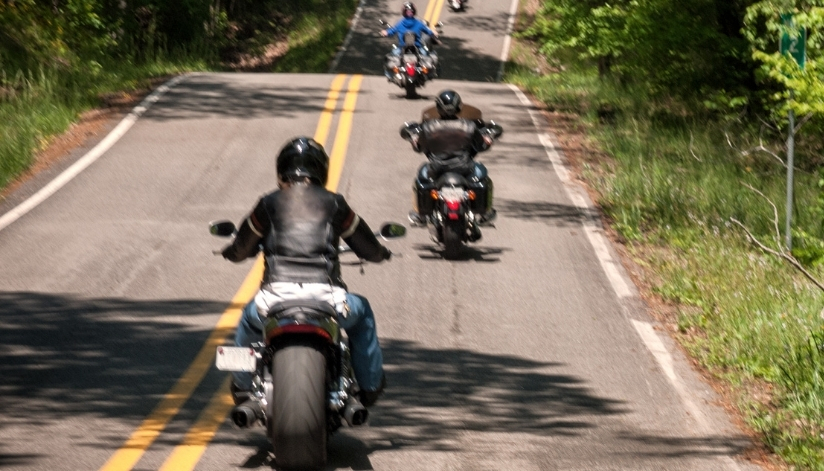 Several motorcyclists riding along a winding two-lane road surrounded by trees.