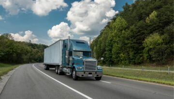 Commercial semitruck traveling on a highway through a wooded area.