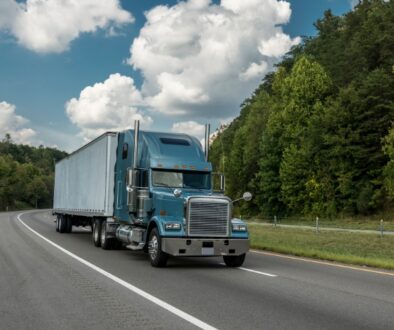 Commercial semitruck traveling on a highway through a wooded area.